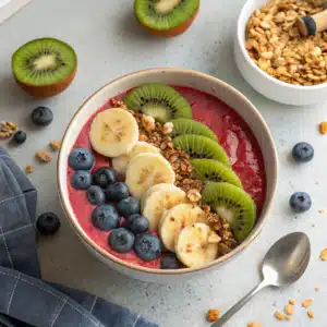Smoothie bowl végan sans sucre garni de fruits frais, graines de chia et coco râpée, présenté dans un bol en céramique clair sur fond naturel.