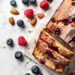 Gâteau aux fruits rouges sans sucre tranché sur une planche en marbre, avec framboises et myrtilles fraîches